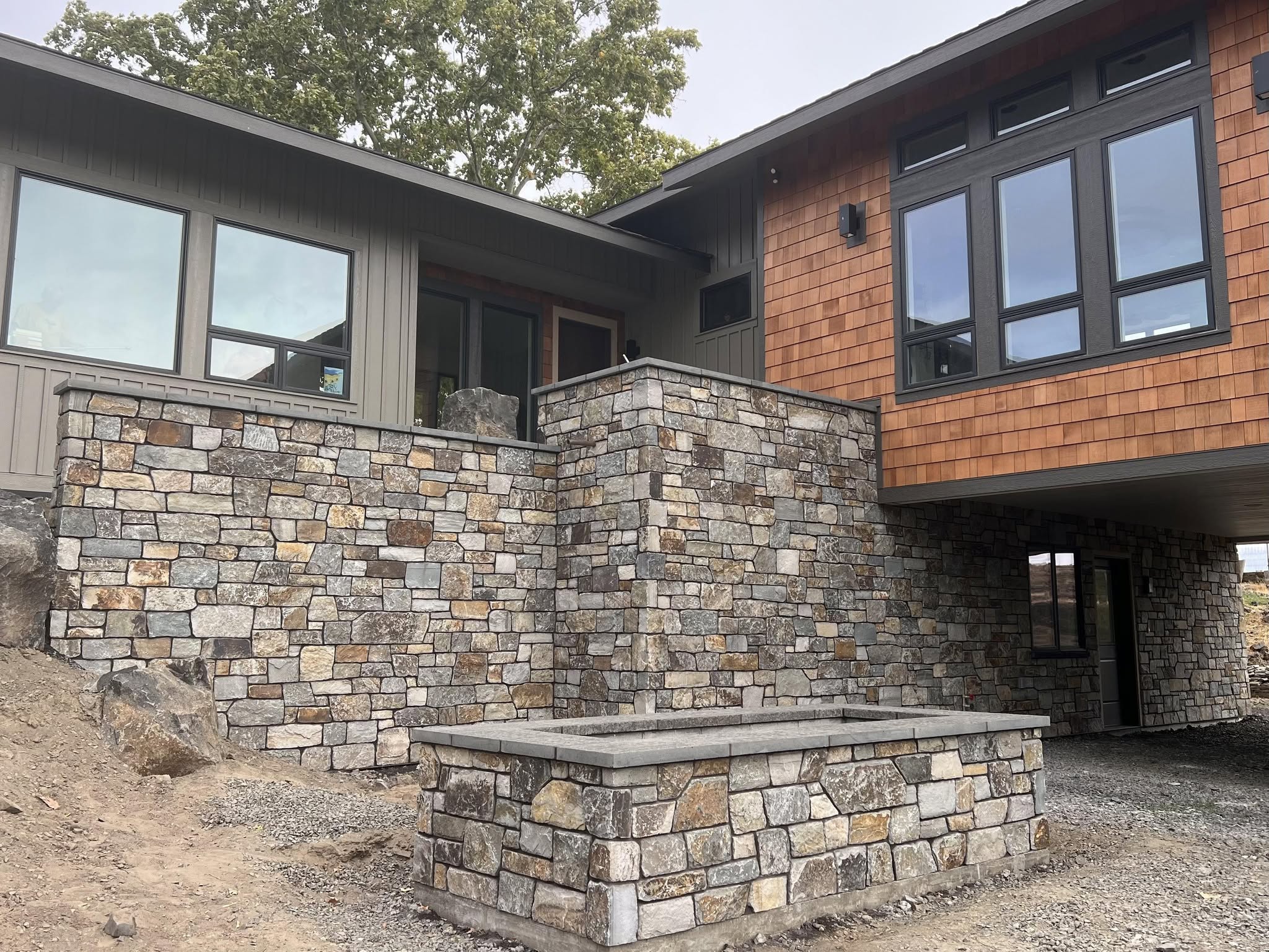 Original Alano Masonry project photograph showing stone walls, a central stone pillar, and cedar siding
